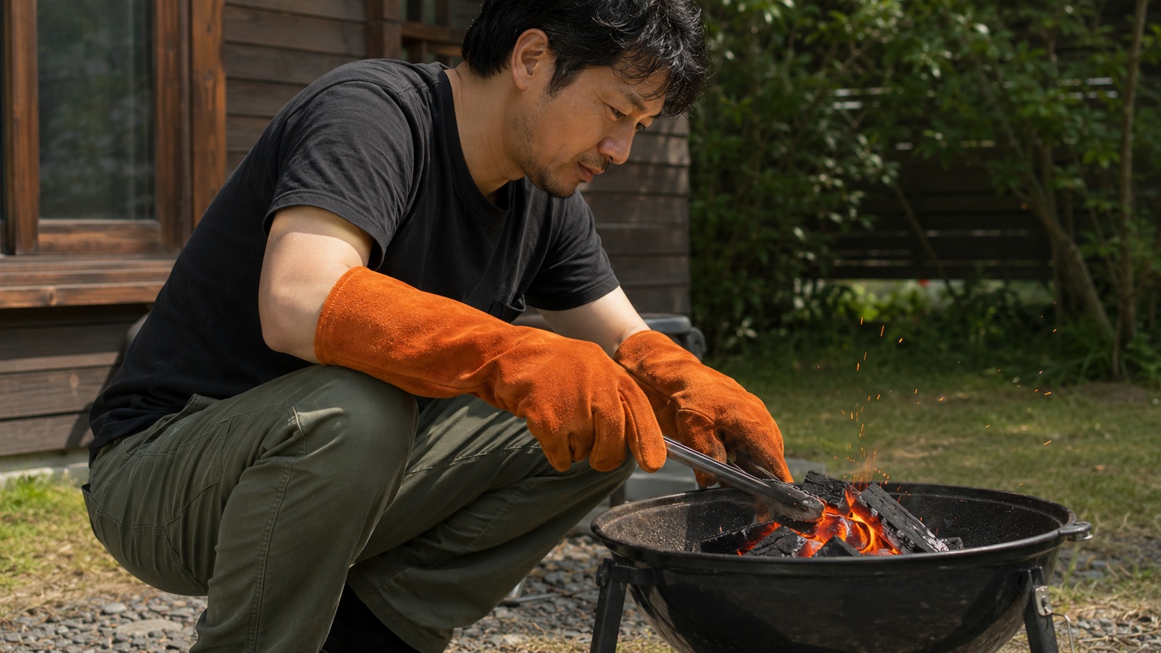 牛革の耐熱グローブでBBQの炭をトングで動かす男性