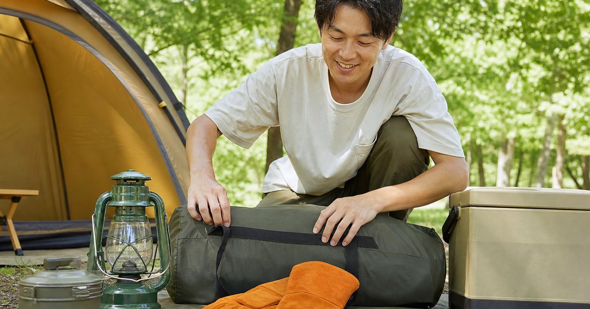 キャンプ場でギアを確認する笑顔の男性と持ち物一式