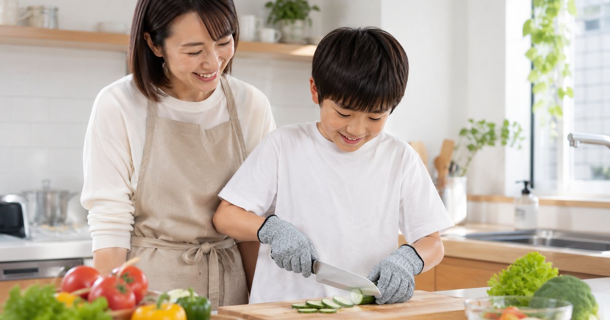 防刃手袋をつけた子供が大人の見守りのもと包丁で野菜を切る様子