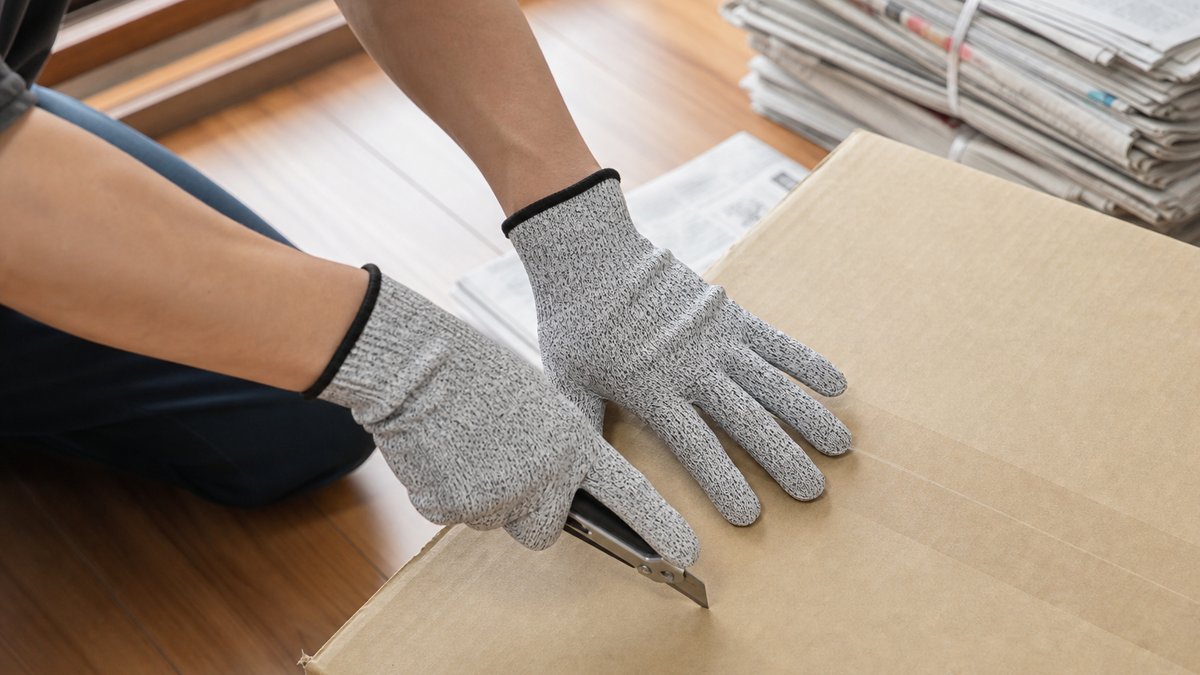 作業用手袋をつけてカッターで段ボールを解体する手元